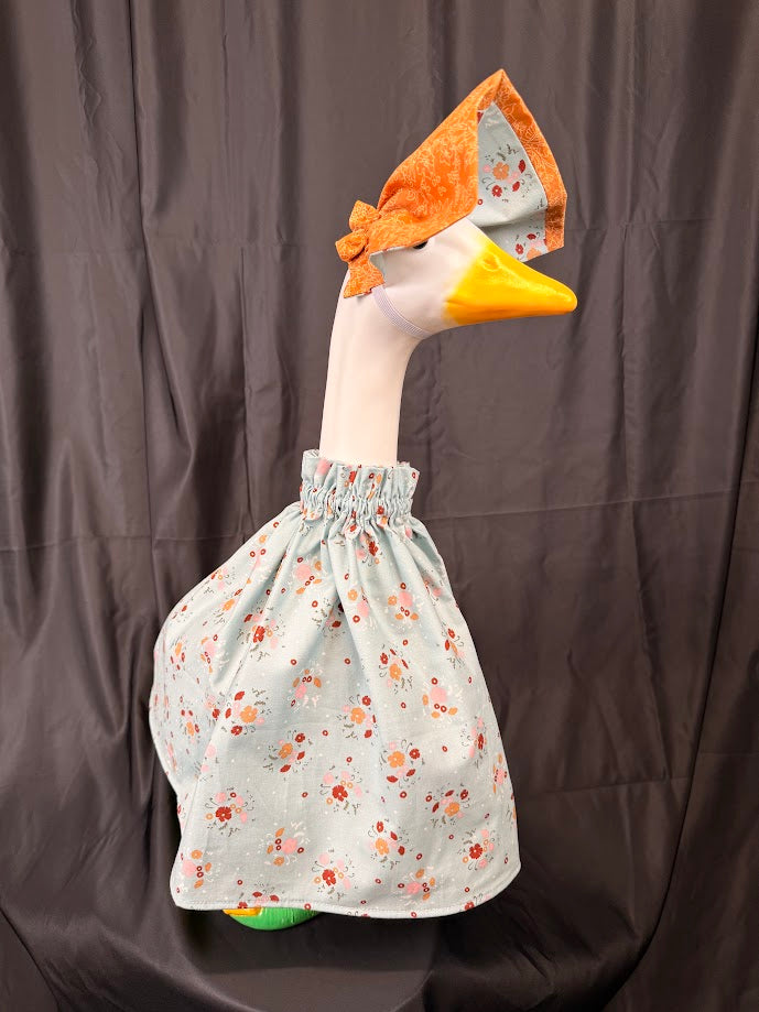 Goose statue wearing blue ditsy floral dress and orange brocade/floral hat – side profile