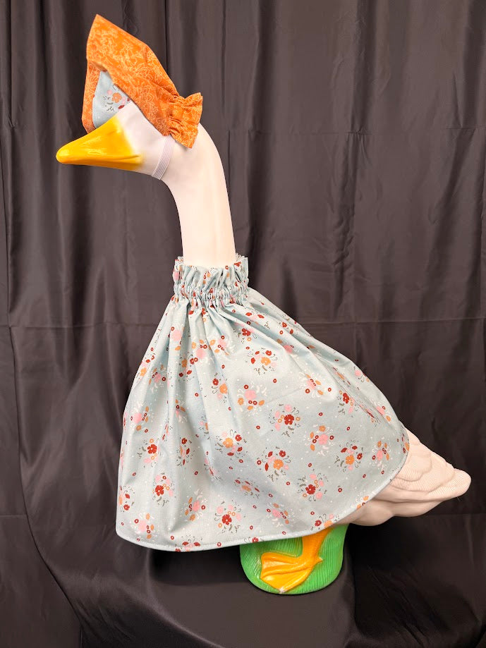 Goose statue wearing blue ditsy floral dress and orange brocade hat – angled side view