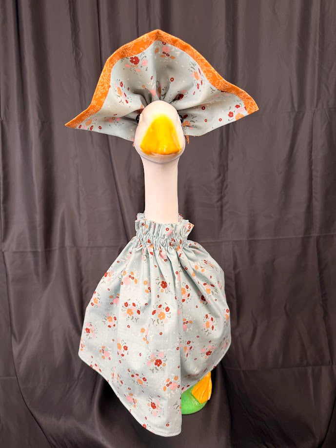 Goose statue wearing blue ditsy floral dress and wide orange brocade hat – front view
