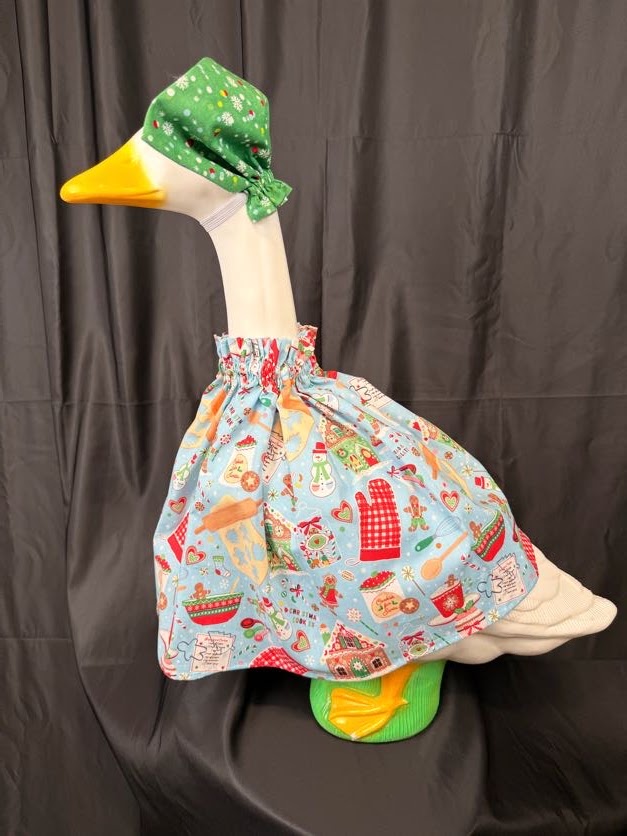 Goose statue wearing light blue Christmas baking dress and green snowflake hat – three-quarter view
