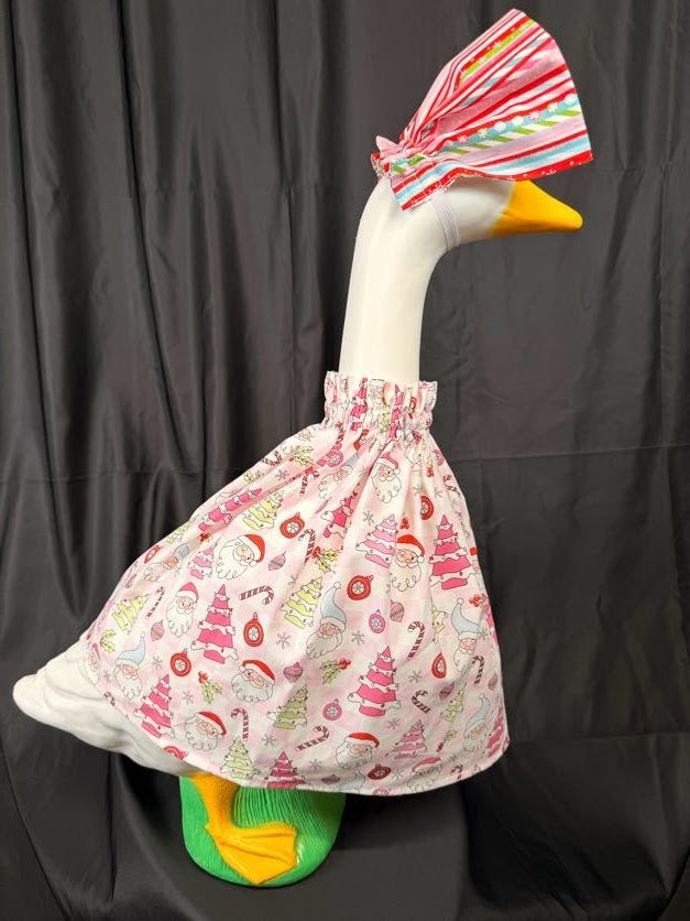 Goose statue wearing pink Christmas print dress and striped hat – side view