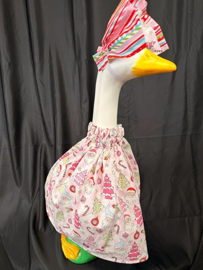 Goose statue wearing pink Christmas print dress and striped hat – angled side view