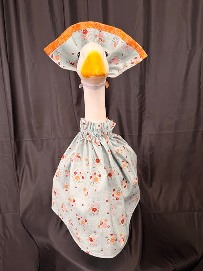 Goose statue wearing blue ditsy floral dress and large orange brocade hat – front view