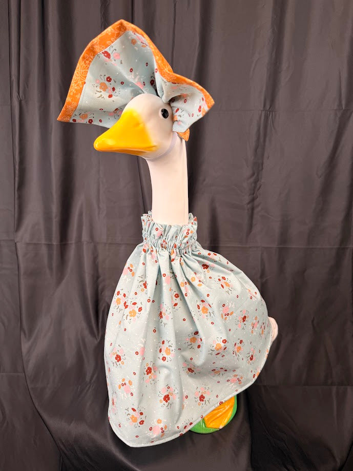 Goose statue wearing blue ditsy floral dress and large orange brocade/floral hat – three-quarter view