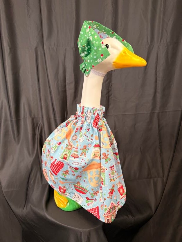Goose statue wearing light blue Christmas baking dress and green hat – angled side view