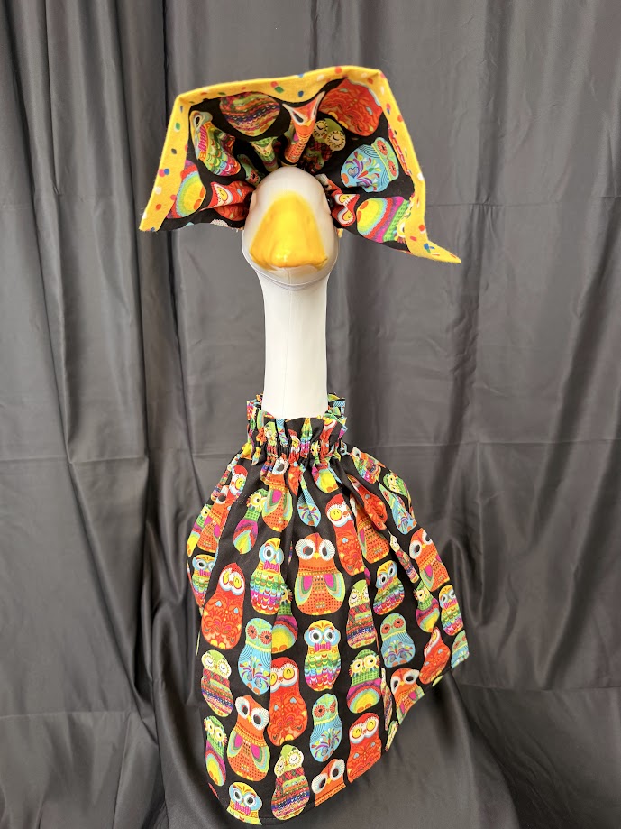 Goose statue wearing black colorful owl print dress and large yellow polka dot hat – front view