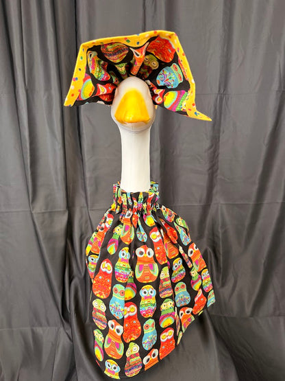 Goose statue wearing black colorful owl print dress and large yellow polka dot hat – front view