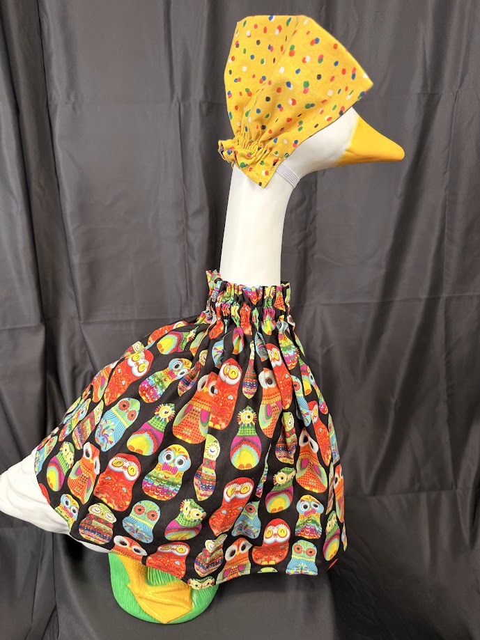 Goose statue wearing black colorful owl print dress and solid yellow polka dot hat – side view