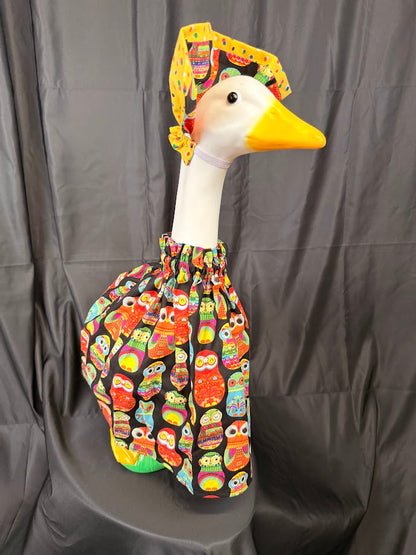 Goose statue wearing black colorful owl print dress and yellow/owl reversible hat – angled side view