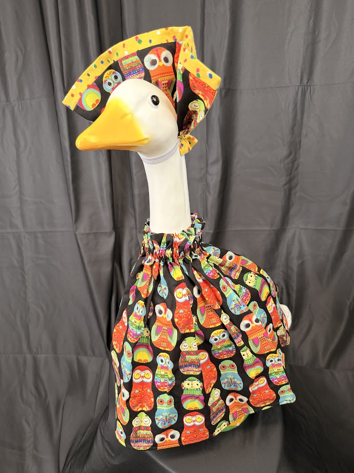 Goose statue wearing black colorful owl print dress and large reversible owl hat – side profile