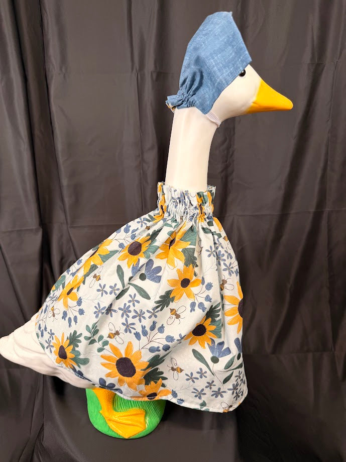 Goose statue wearing white sunflower bee botanical dress and solid blue chambray hat – side view