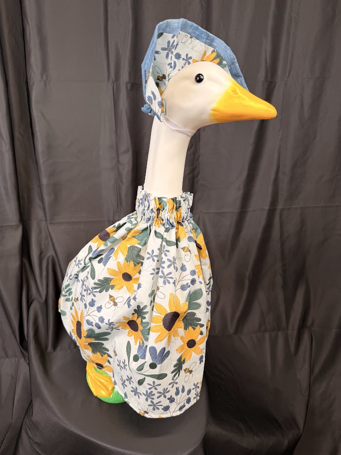 Goose statue wearing white sunflower bee botanical dress and blue chambray/sunflower hat – angled side view